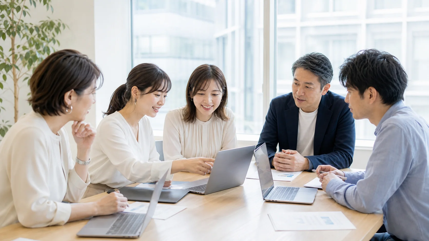 明るい自然光の会場で、女性メンバーを中心に男女の参加者がノートPCを囲んで相談する様子