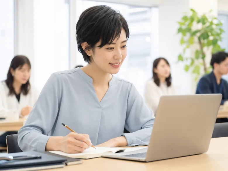 明るいセミナールームでメモを取りながら学ぶ20代後半の日本人女性参加者のイメージ